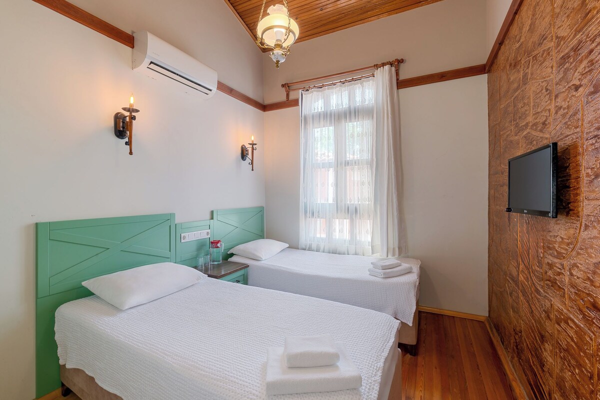 A hotel room with two beds, a TV, an air conditioner, and a window with sheer curtains.