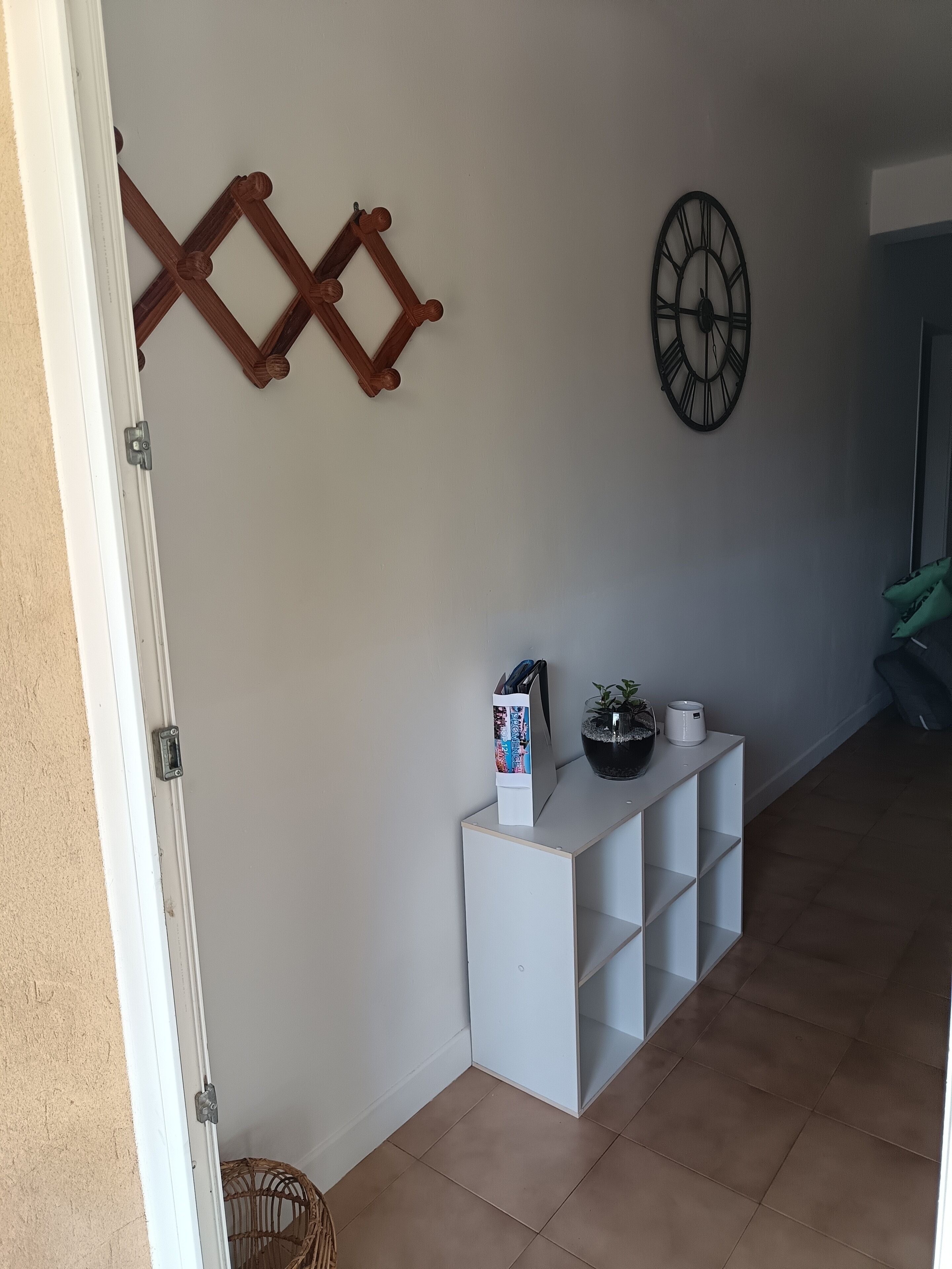 Un pasillo con una consola blanca, un reloj de pared y una celosía de madera decorativa.