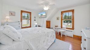 Un dormitorio con cama, escritorio, silla y televisor en la pared.