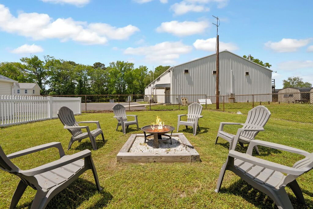 A backyard with a fire pit, four Adirondack chairs, and a white barn in the background.