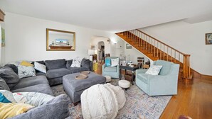 Una sala de estar con un sofá seccional gris, un sillón azul claro y una escalera de madera.
