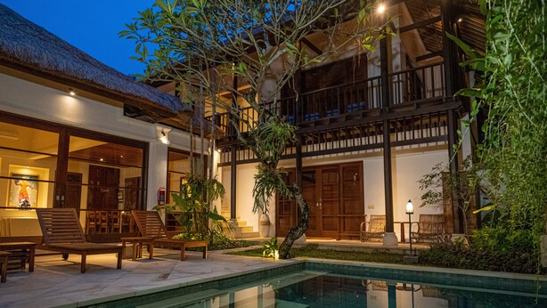 Un área junto a la piscina con sillones de descanso, una piscina pequeña y un edificio con techo de paja y balcones de madera.