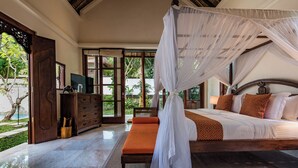 Un dormitorio con cama con dosel, un banco de madera y vistas del jardín por la puerta.