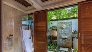Un baño moderno con cabina de ducha de vidrio, puerta de madera y pared de piedra con fuente de agua.