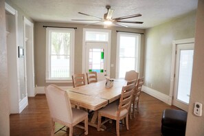A dining room with a wooden table and chairs, a ceiling fan, and large windows. - Relaxing Home W/HUGE Yard & Firepit! (Junction)