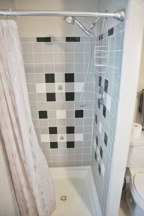A shower area with a tiled wall, a showerhead, and a curtain. - Relaxing Home W/HUGE Yard & Firepit! (Junction)