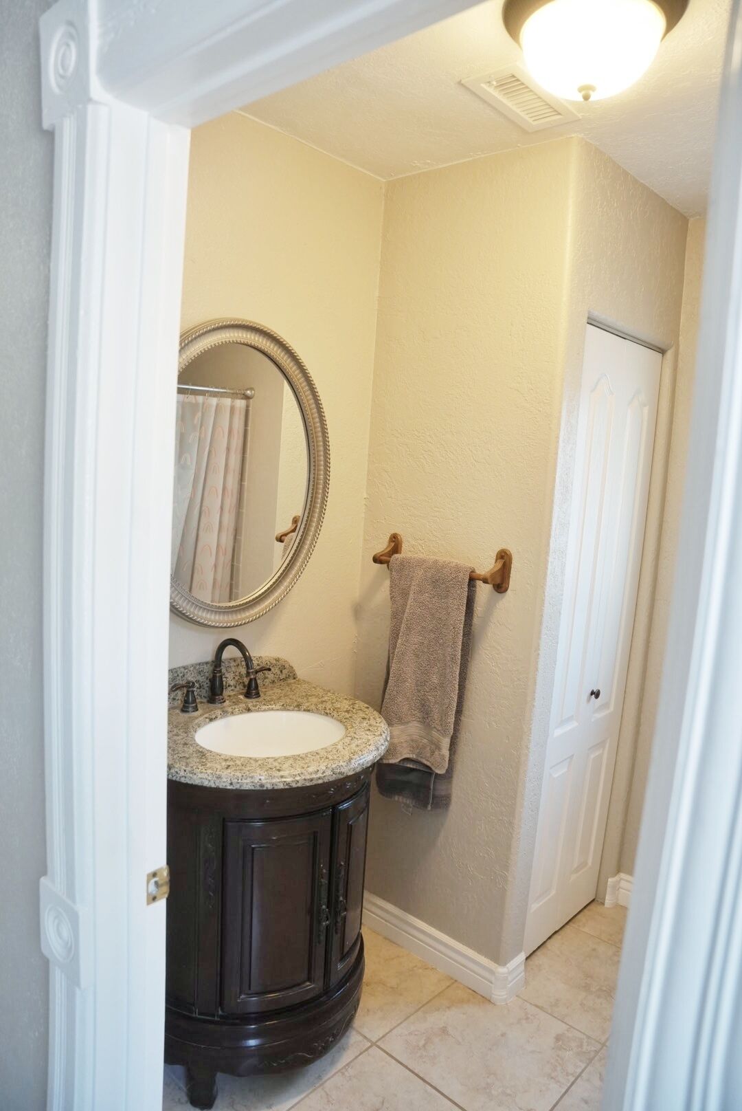 A bathroom with a vanity, sink, mirror, towel rack, and door.