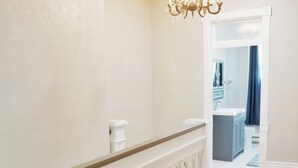 Un pasillo amplio con suelo de madera, barandilla blanca y un candelabro.