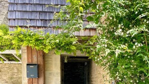 A narrow alleyway with a wooden door leading to a dark interior, surrounded by greenery and a stone wall. - "La Victoire" Fisherman's house at an alleyway from the sea... (Saint-Aubin-sur-Mer)