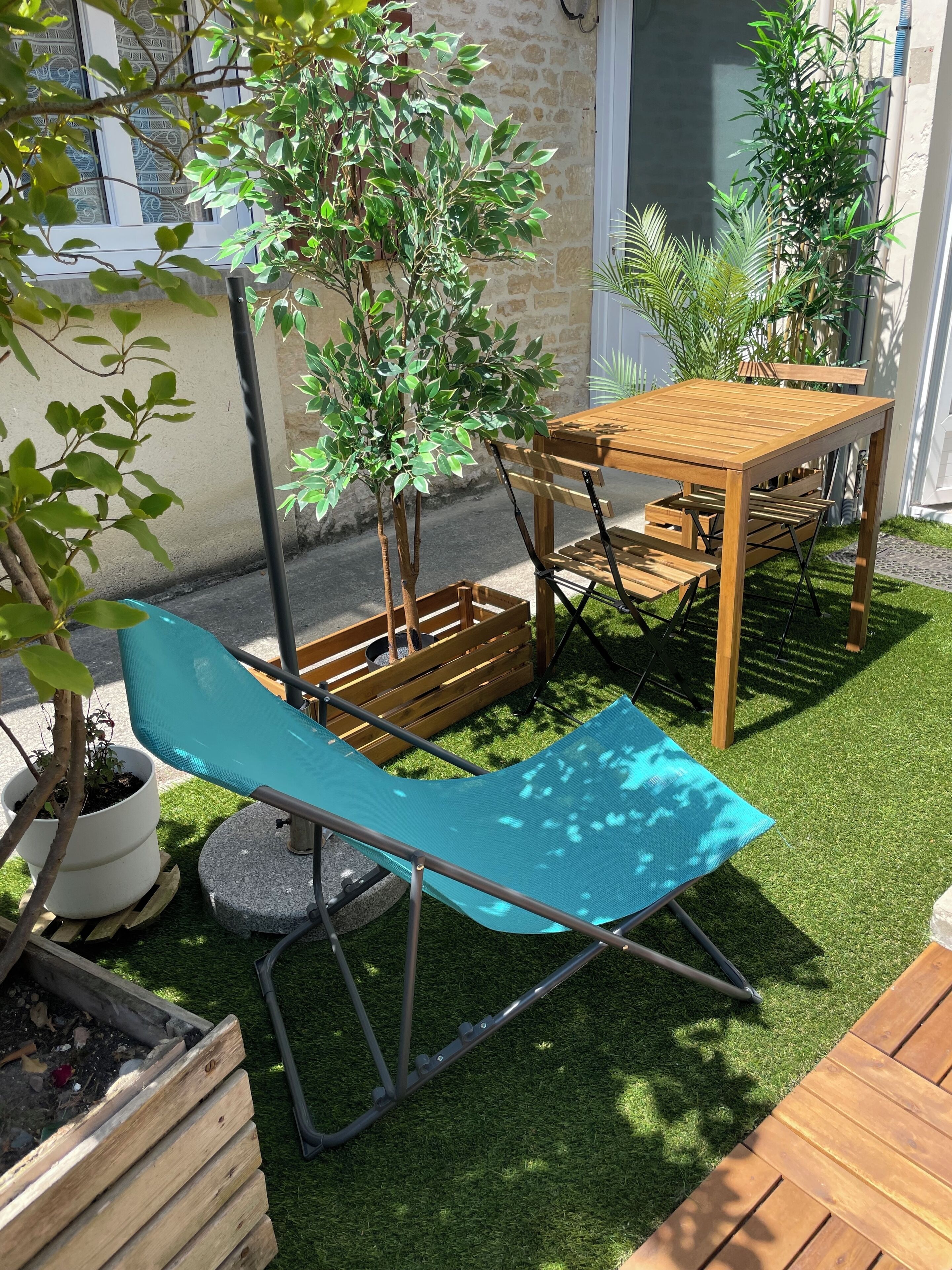 Een terras met een houten tafel en stoelen, omringd door potplanten en een kleine boom.