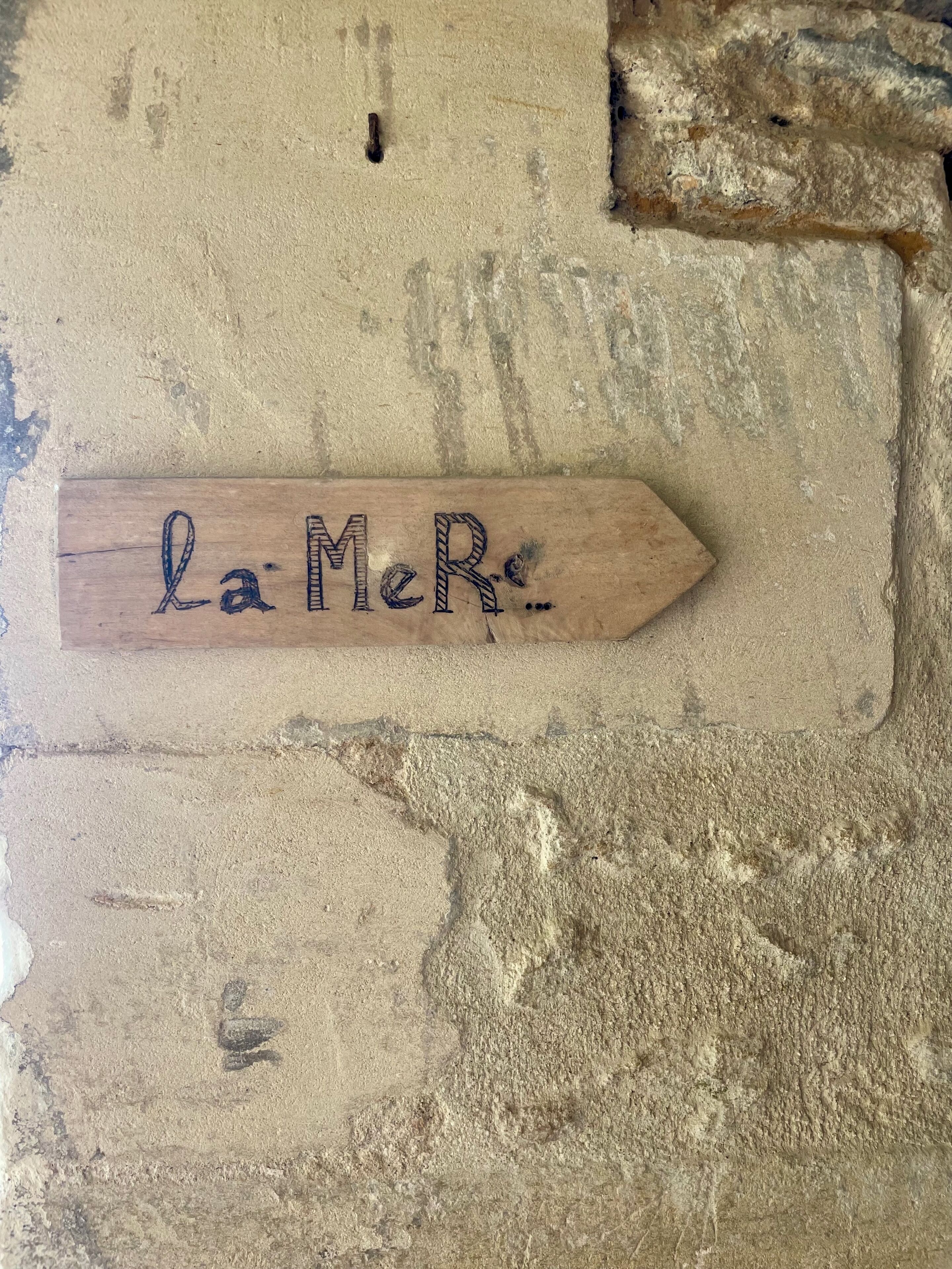 Une enseigne en bois portant l’inscription « La Mer », fixée à un mur à texture.
