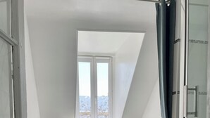 A bedroom with a bed, a window, and a shower area. - "La Victoire" Fisherman's house at an alleyway from the sea... (Saint-Aubin-sur-Mer)