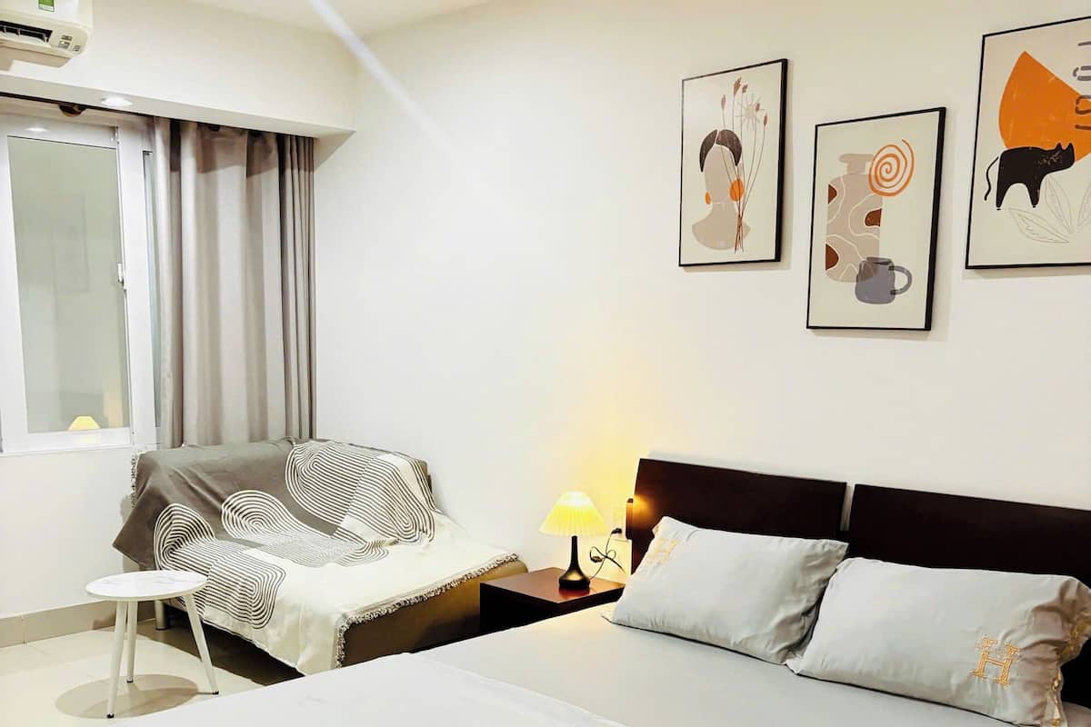 A hotel room with a large bed, a sofa, a small table, and a window with curtains.