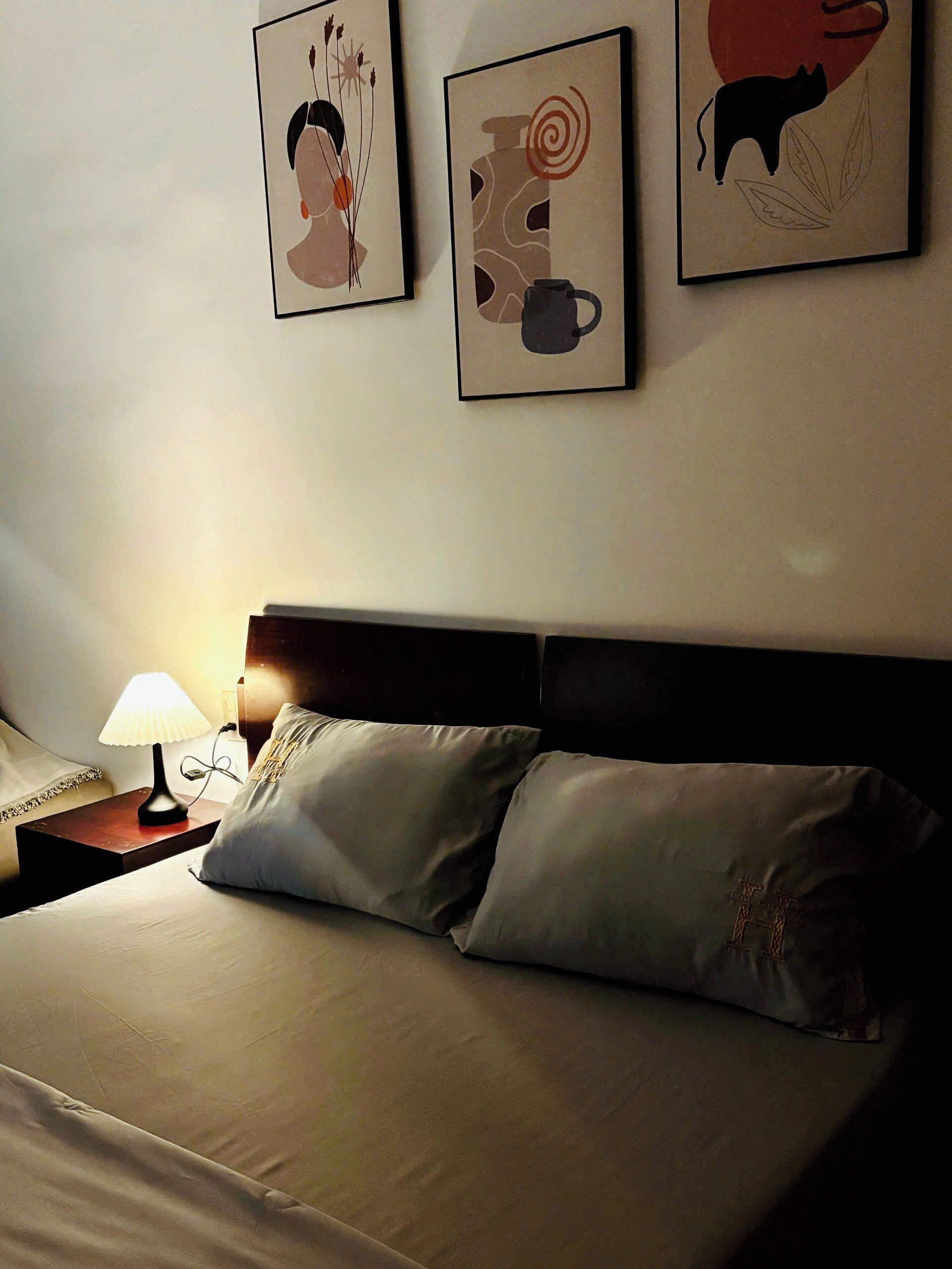 Una habitación de hotel con una cama, dos almohadas, una mesita de noche con una lámpara y tres cuadros en la pared.