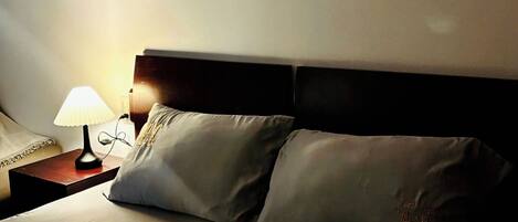 Una habitación de hotel con una cama, dos almohadas, una mesita de noche con una lámpara y tres cuadros en la pared.