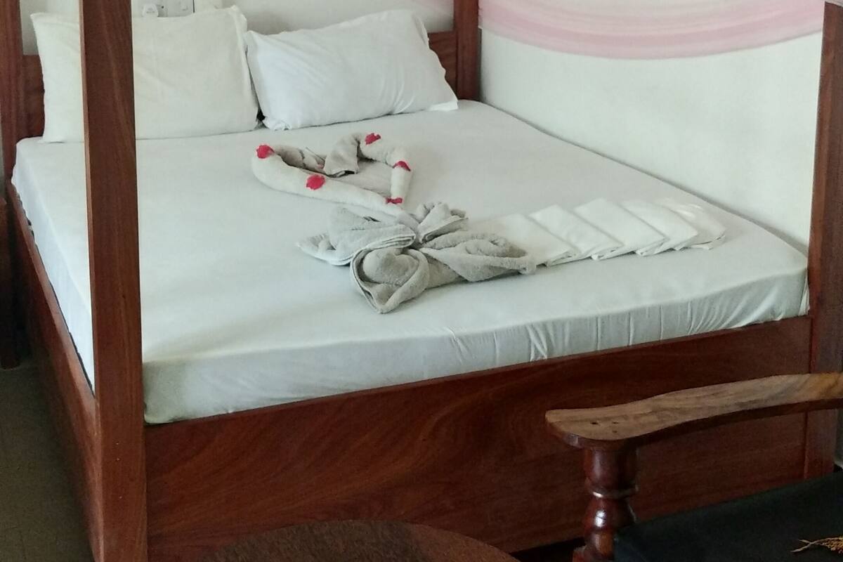 Una cama con dosel y cuatro columnas, una mesita de noche de madera y una pequeña mesa redonda.