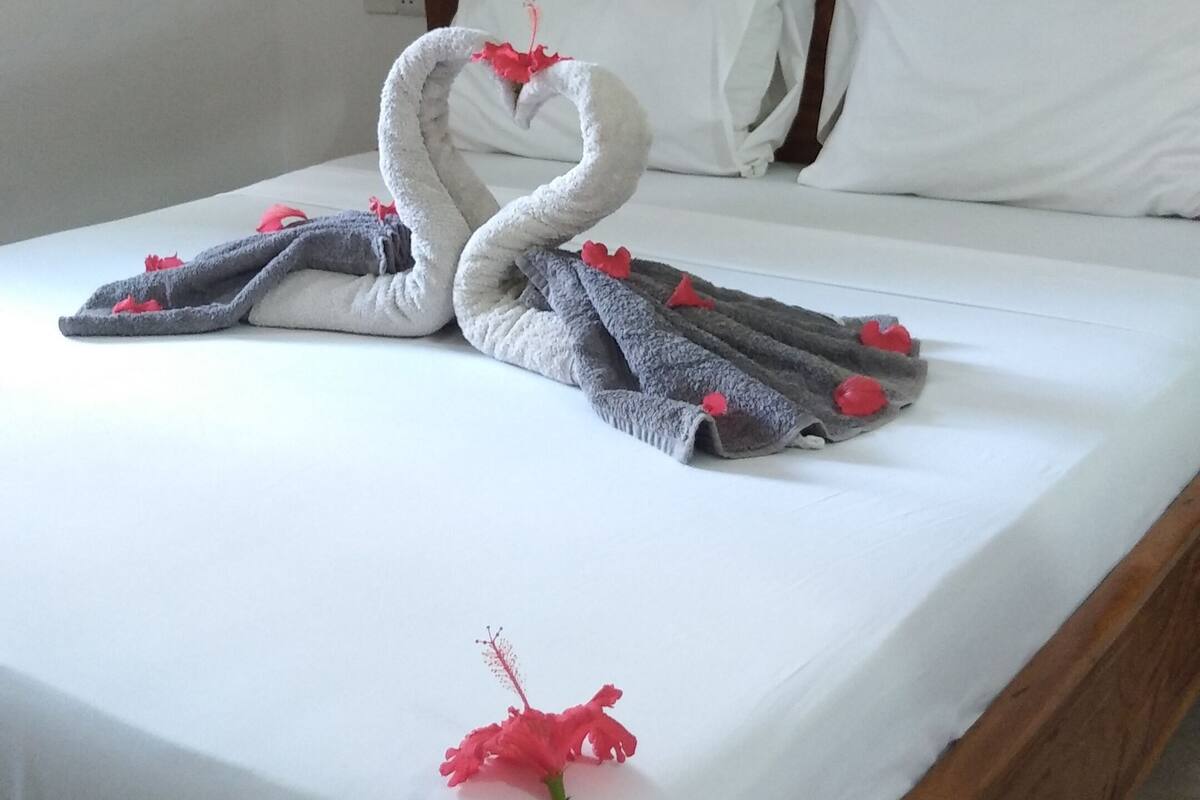 Una cama con cabecera de madera, ropa de cama blanca y una decoración de toallas con forma de cisne.