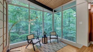 A room with large windows, two chairs, a small table, and a floor lamp.