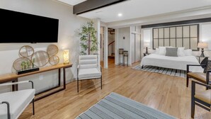 A modern hotel room with a large bed, a desk, a chair, a TV mounted on the wall, and a potted plant.
