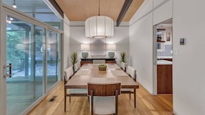 A modern dining room with a large wooden table, white walls, and a ceiling with a woven design.