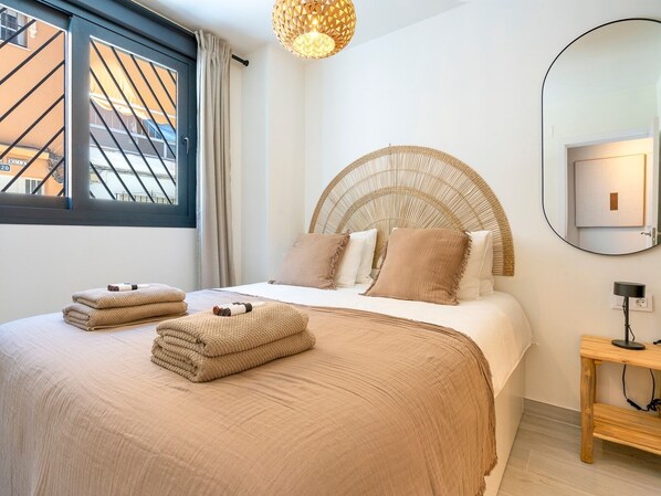 A bedroom with a bed, a bedside table, a mirror, and a window with curtains.