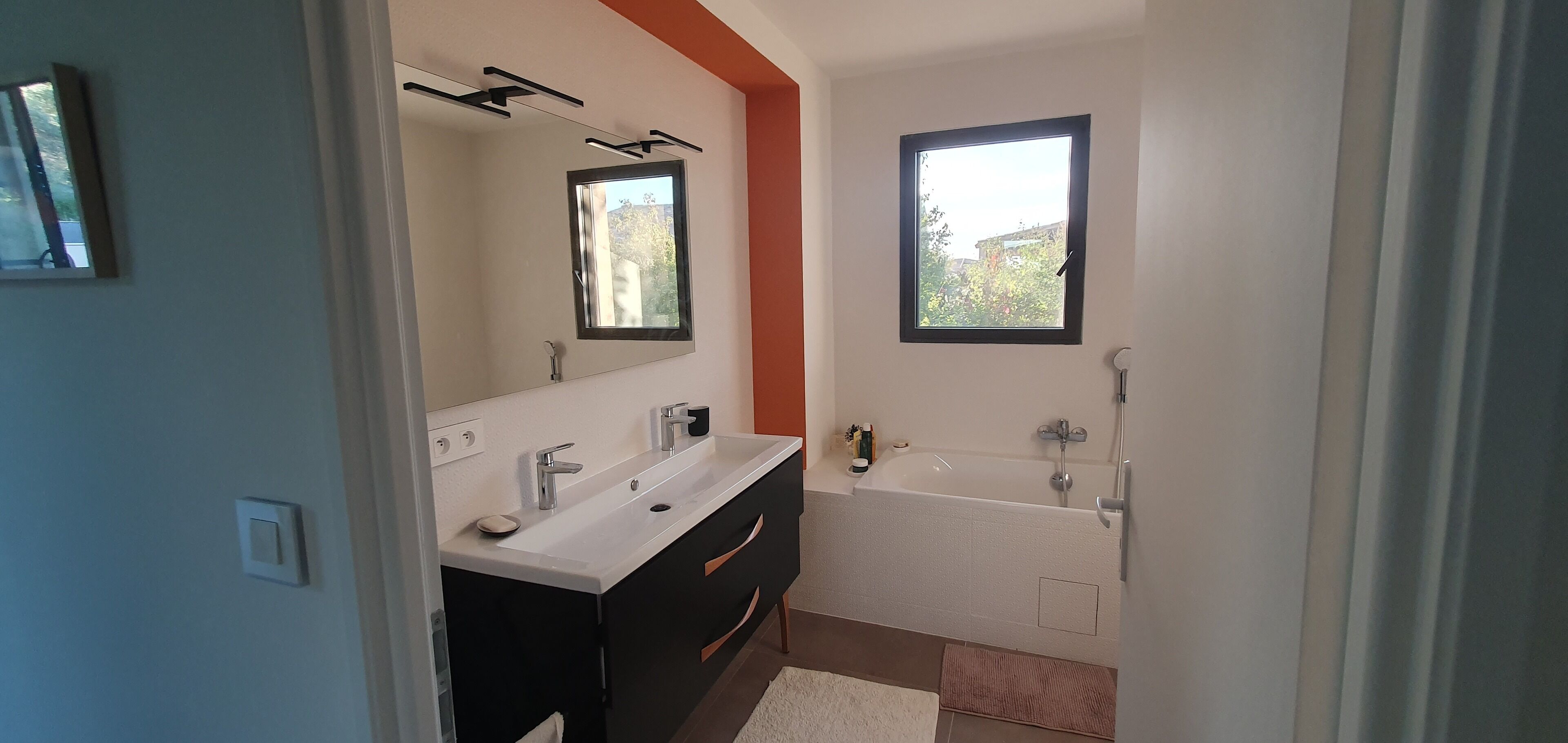 A modern bathroom with a double sink vanity, a bathtub, and a large mirror.