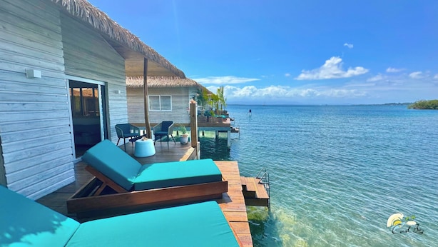 An overwater bungalow with a thatched roof, wooden deck, and lounge chairs. - Coral Reef Over Water Bungalow, Bedroom, King Bed, Living Room, Kitchenette (Bastimentos Island)