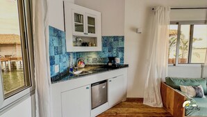 A compact kitchen with a built-in dishwasher, a coffee machine, and a window with a view of a thatched-roof structure. - Coral Reef Over Water Bungalow, Bedroom, King Bed, Living Room, Kitchenette (Bastimentos Island)