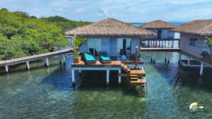 Overwater bungalows with thatched roofs, wooden walkways, and clear blue water. - Coral Reef Over Water Bungalow, Bedroom, King Bed, Living Room, Kitchenette (Bastimentos Island)