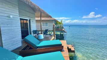 Un bungalow sur pilotis doté d’un toit de chaume, d’une terrasse en bois et de chaises longues.