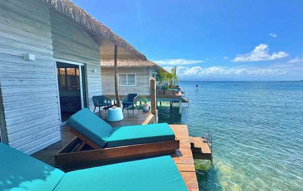 Un bungalow sur pilotis doté d’un toit de chaume, d’une terrasse en bois et de chaises longues.