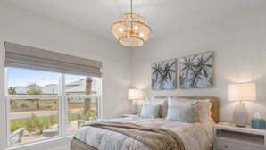 A bedroom with a large bed, bedside tables, a window with a view, and a ceiling light fixture. - The Tipsy Turtle- Port St. Joe/Windmark Beach + Pet Friendly (Port St. Joe)