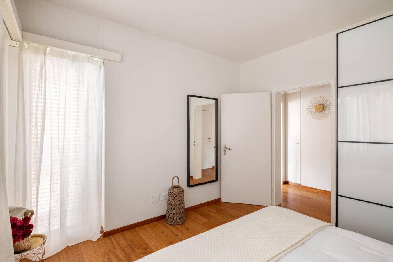 Une chambre à coucher avec un lit, un miroir, une porte et une horloge murale.