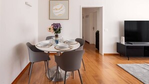 Un comedor moderno con una mesa redonda dispuesta para cuatro personas, rodeada de sillas grises. Un jarrón con flores está sobre la mesa, y una obra de arte enmarcada cuelga en la pared de arriba.