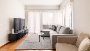 Una sala de estar moderna con un televisor de pantalla plana, un sofá gris, una mesita de centro y cortinas ligeras.
