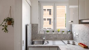 Una cocina moderna con encimera de granito, pileta de acero inoxidable y ventana con vista a un edificio de ladrillo.