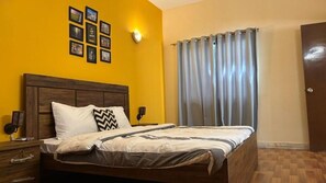 A bedroom with a wooden headboard, a bed with a striped bedspread, a nightstand with a lamp, and a wall with framed pictures. - Heavenly Stays  (Karachi)