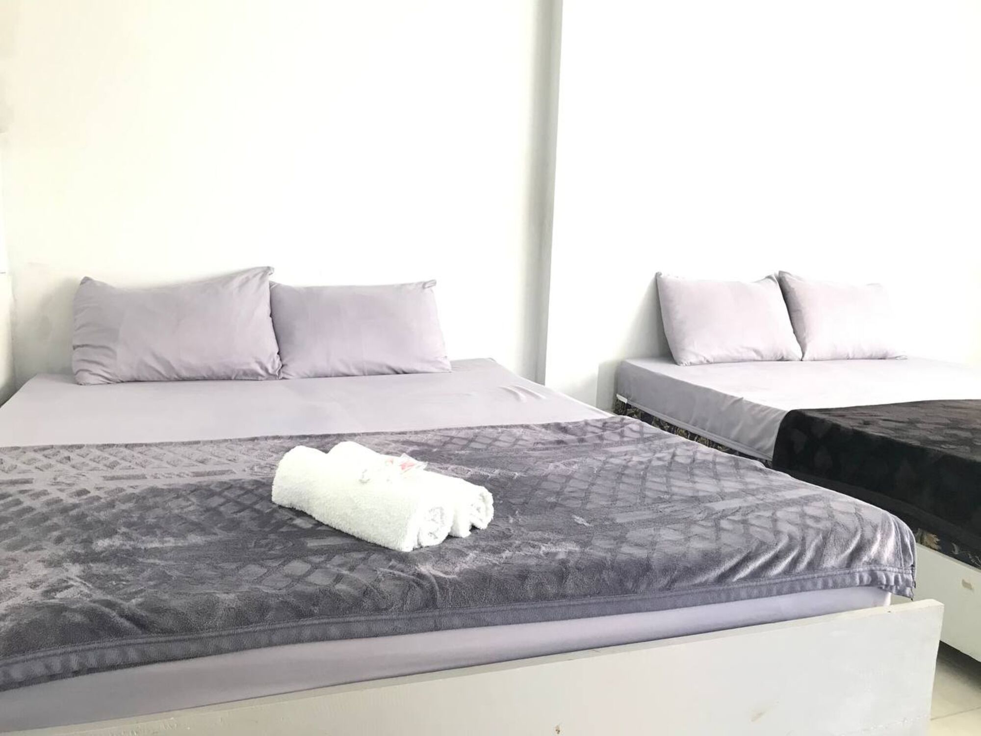 Two single beds with grey bedding and a rolled towel on the bed in the foreground.