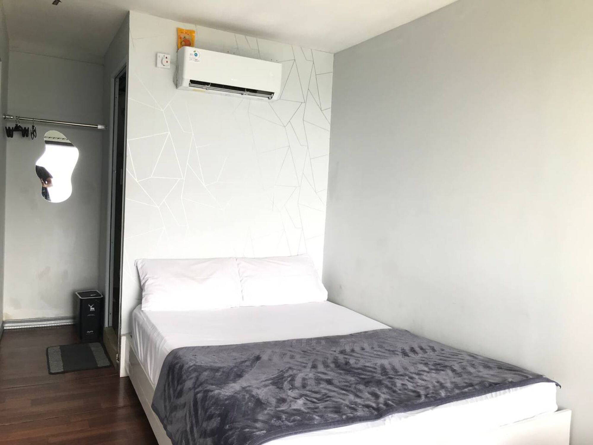 Un dormitorio moderno con una cama, un aire acondicionado de pared, un perchero y un cubo de basura pequeño.