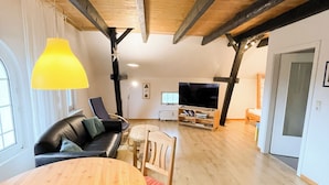 Ein großzügiger Wohnbereich mit Holzboden, einem runden Holztisch, einer Couch und einem Fernseher.