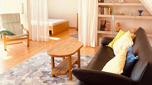 Ein gemütliches Wohnzimmer mit einer schwarzen Couch, einem Holztisch, einem Sessel und einem Bücherregal.
