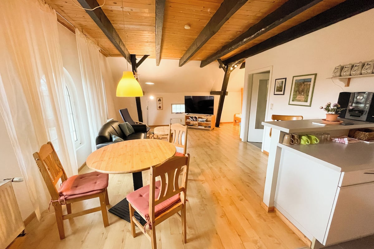 Ein gemütliches Wohnzimmer mit einem Holzesstisch, zwei Stühlen, einer Couch und einem Fernseher.