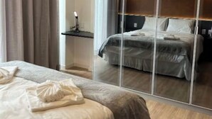 A hotel room with a large mirror, a bed with a white comforter, and a wooden floor. - Hotel Boutique Gran Paradiso Resort (Campos do Jordão)