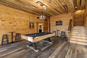Un intérieur en bois avec une table de billard, des tabourets et un escalier.