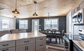 Cozinha moderna com teto de madeira, bancada de mármore e área de refeições com mesa e cadeiras.