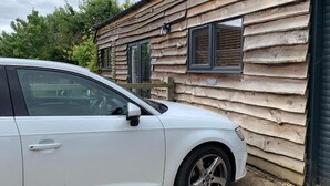 A white car parked in front of a rustic wooden cabin with two windows and a door. - Cozy barn conversion within minutes from Silverstone. (Towcester)