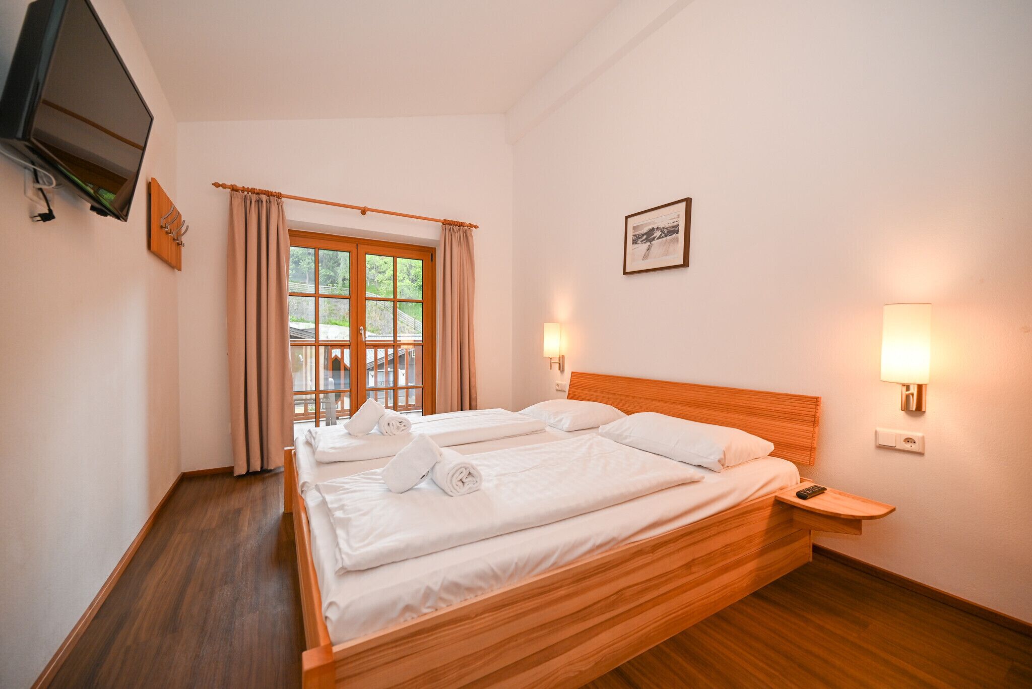 Una habitación de hotel con una cama de madera, un televisor montado en la pared y una ventana con cortinas.