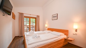 Ein Hotelzimmer mit einem hölzernen Bett, einem an der Wand befestigten Fernseher und einem Fenster mit Vorhängen.