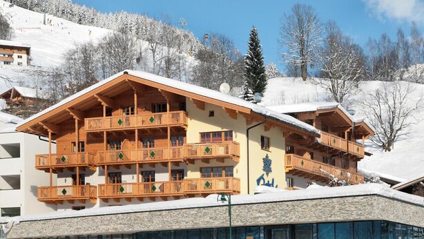 Ein mehrstöckiges Holzgebäude mit Balkonen, umgeben von schneebedeckten Bäumen und wolkenlosem Himmel.