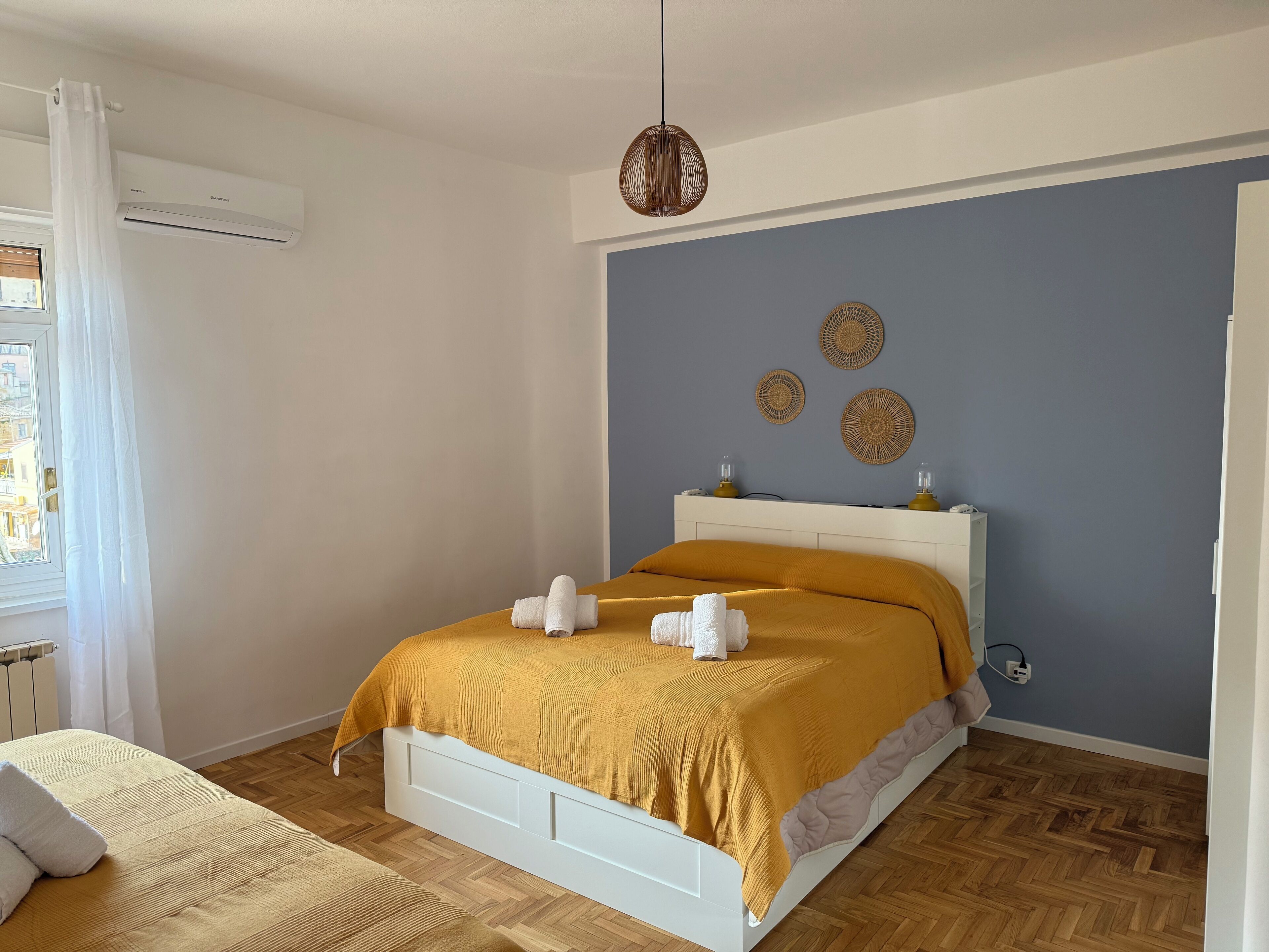 A bedroom with a bed, a window with curtains, an air conditioner, and a wall with decorative items.